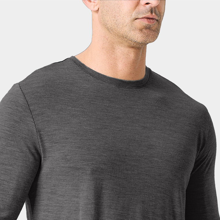 Male model wearing a lightweight Merino wool long sleeve crew base layer top, breathable and comfortable, shown in dark grey heather.