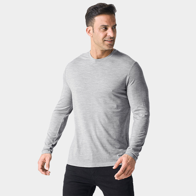 Male model wearing a lightweight Merino wool long sleeve crew base layer top, breathable and comfortable, shown in light grey heather.