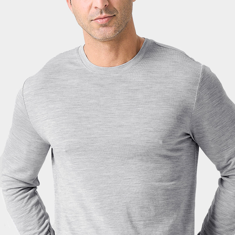 Male model wearing a lightweight Merino wool long sleeve crew base layer top, breathable and comfortable, shown in light grey heather.