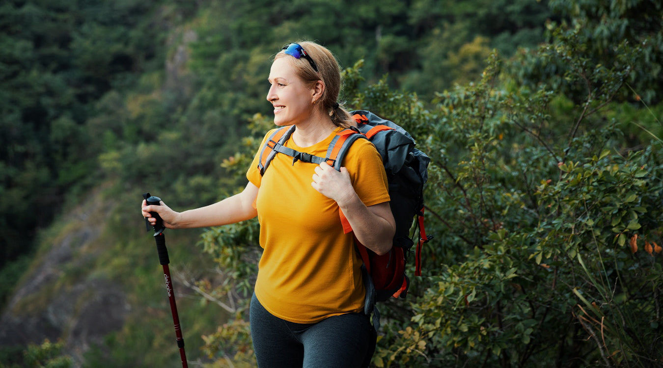 Woman wearing merino t shirt hiking with a backpack and walking stick in a forest